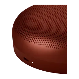 Bang & Olufsen BeoSound A1 3rd Gen rojo, detalle lateral: rejilla perforada y botón en la base sobre fondo oscuro