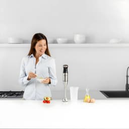 Taurus Mixeur BAPI 1500 Inox, scène cuisine: femme préparant une recette à côté du mixeur plongeant inox sur le plan de