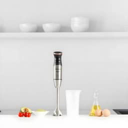 Taurus Mixeur BAPI 1500 Inox, vue en scène: mixeur plongeant vertical sur plan de travail avec avocat, tomates, œufs et huile