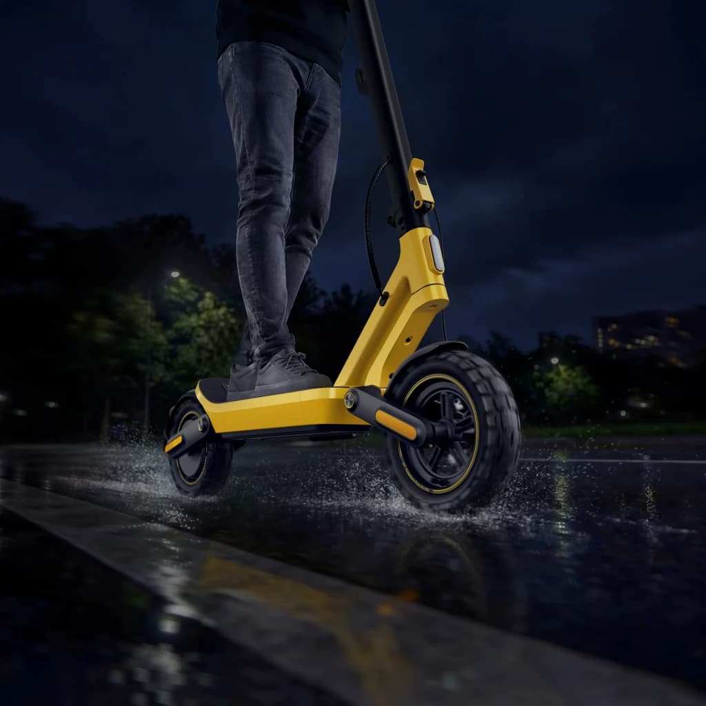 Xiaomi Electric Scooter 6 Ultra GL Noir Jaune, vue latérale basse: personne roulant de nuit sous la pluie, éclaboussures sur