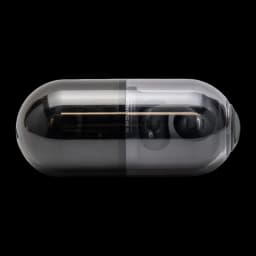 Boîtier ovale fumé et brillant abritant les écouteurs Moondrop Pill OWS Noir, coque translucide grise laissant voir les clips d’oreille compacts