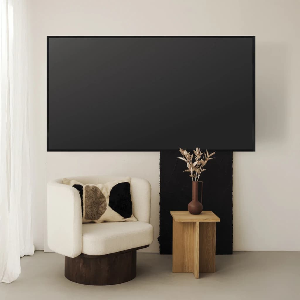 TooQ LP1050F-B Soporte TV Fijo Negro, vista en sala: TV grande montada en pared sobre sillón blanco y mesa auxiliar madera