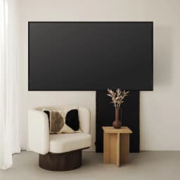 TooQ LP1050F-B Soporte TV Fijo Negro, vista en sala: TV grande montada en pared sobre sillón blanco y mesa auxiliar madera