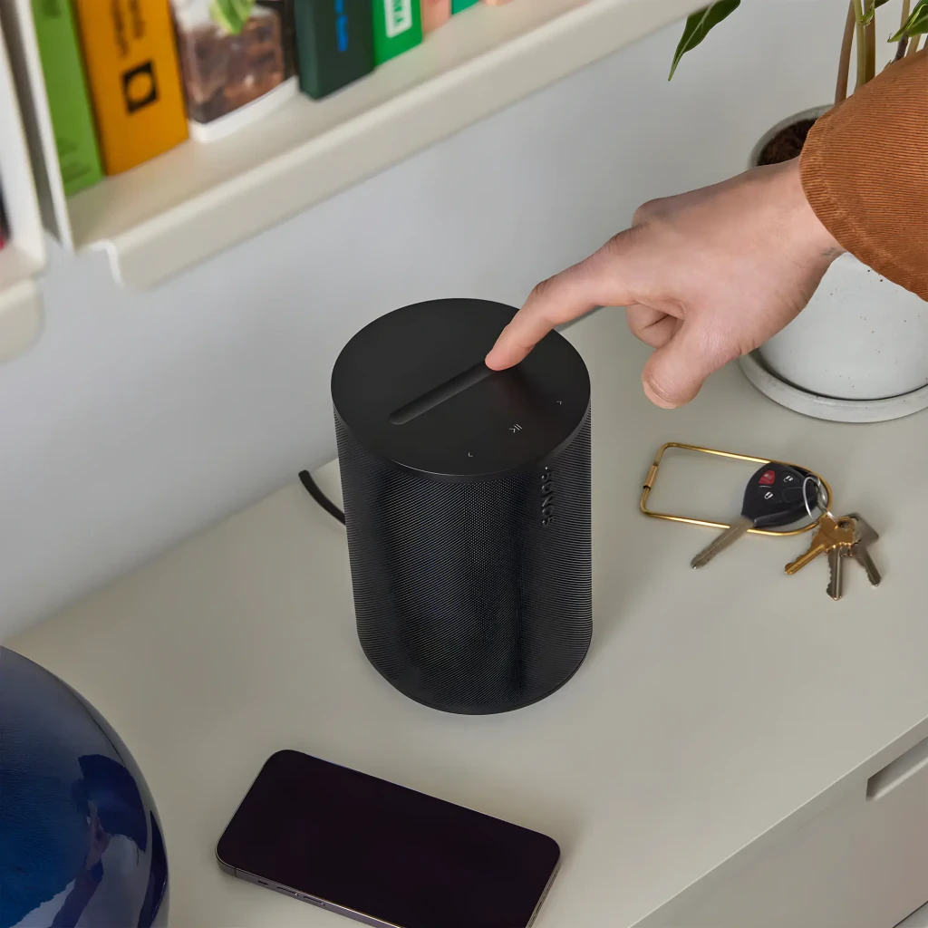 Sonos Era 100 SL noir, usage: main sur panneau tactile supérieur posé sur bureau avec clés et smartphone