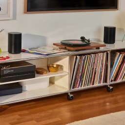 Sonos Era 100 SL noir, vue lifestyle: deux enceintes sur meuble avec platine vinyle et collection de disques