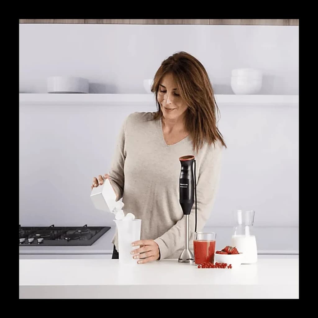 Taurus Bapi 1200 Pure Plus preto, uso na cozinha: mulher preparando batido com varinha mágica ao lado de frutas vermelhas