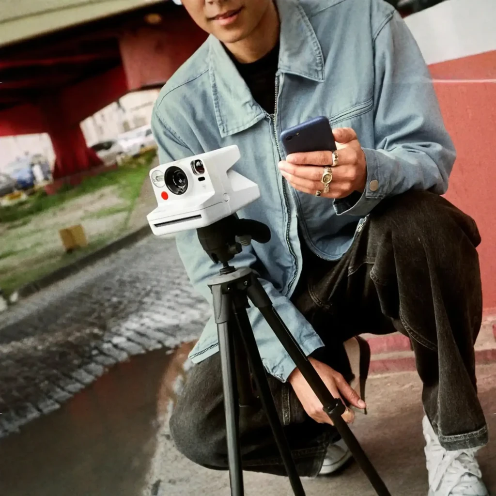 Polaroid Now+ Gen 3 blanca, vista frontal en ángulo: objetivo, flash, botón rojo y franja arcoíris - Ítem4