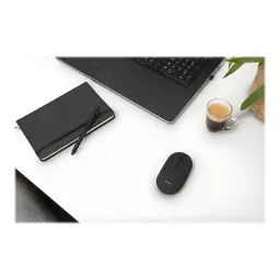 Trust Souris Puck Sans Fil Rechargeable noir, vue lifestyle: sur bureau blanc avec ordinateur portable, carnet et café