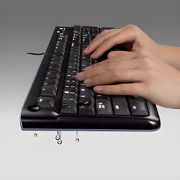 Teclado Logitech K120 USB con cable, diseño QWERTY de tamaño completo en negro, teclas elevadas y perfil inclinado; manos escribiendo sobre las teclas