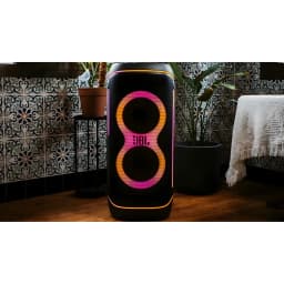 JBL PartyBox 720 800W noir, vue de face en ambiance: lumières LED orange et rose allumées sur table en bois