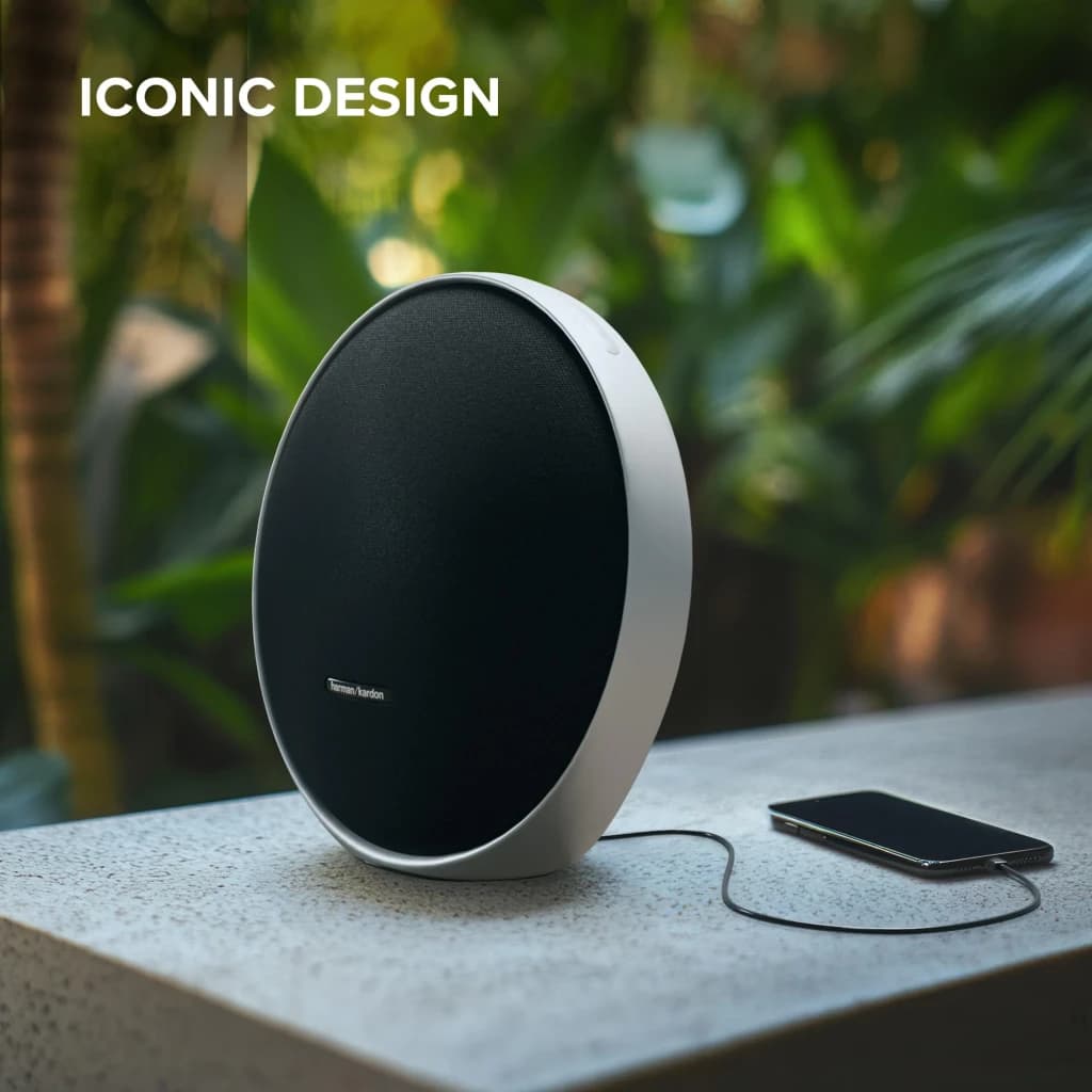 Harman Kardon Onyx Studio 9 negro, vista frontal en exterior: diseño circular con rejilla negra y smartphone conectado por