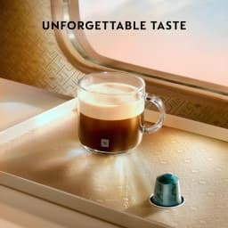 Krups Nespresso Essenza Mini noir, style de vie: tasse en verre avec café et crème à côté d'une capsule verte sur surface