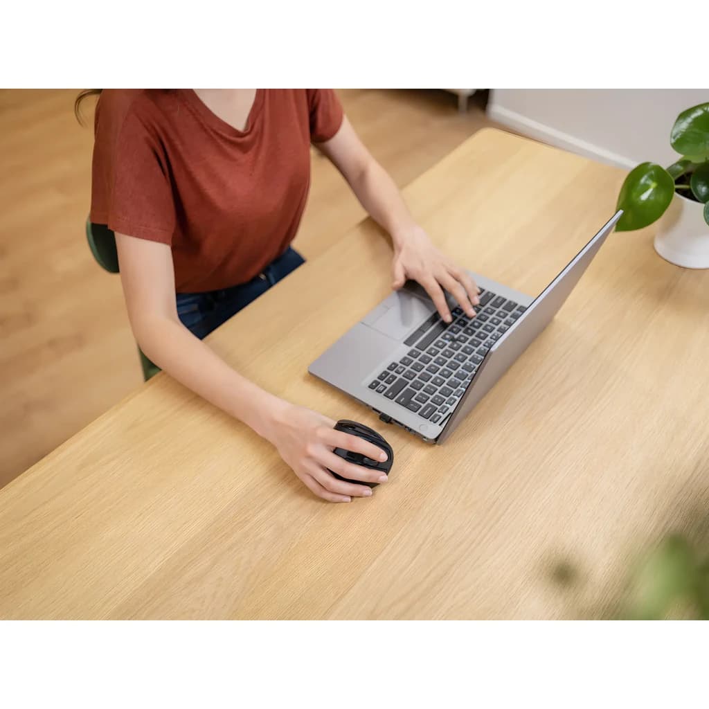 Trust Voxx Ratón Ergonómico Negro, uso en escritorio: mujer sujetando el ratón junto a portátil plateado sobre mesa de madera