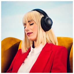 Panasonic RB-HX330B Preto, uso: mulher com auriculares postos relaxada em poltrona mostarda, concha e arco visíveis