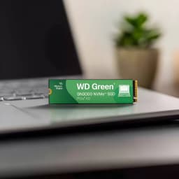 WD Green SN3000 500GB verde, vista lateral: SSD M.2 apoiado em laptop, etiqueta verde com logo e conector dourado visível