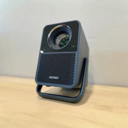 Ultimea Poseidon E40 1000 ANSI 4K 8GB gris, vista frontal en ángulo: lente, rejilla altavoz y asa sobre mesa de madera