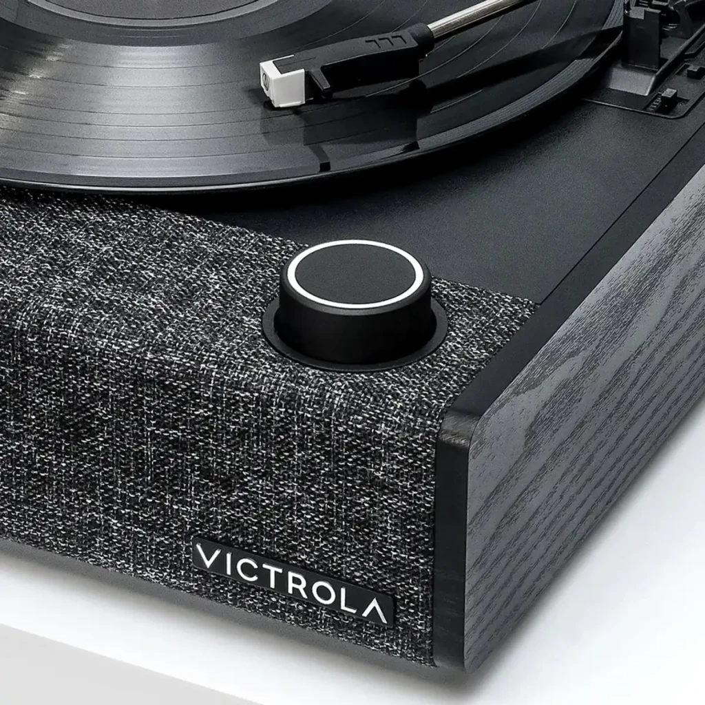 Tocadiscos Victrola Eastwood II VTA-74 con tapa transparente, plato negro, brazo recto y base textil gris; perilla frontal y logotipo Victrola visibles - Ítem4