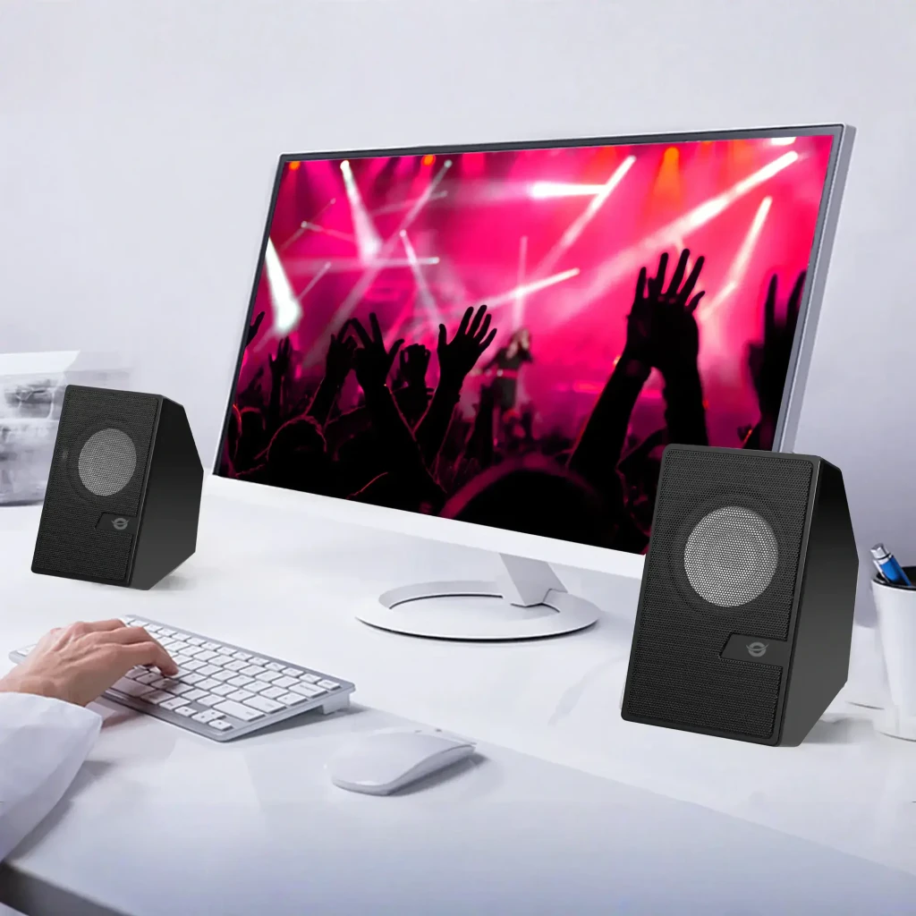 Conceptronic Enceintes 2.0 10W BT USB 3.5mm Noir, vue bureau: paire d'enceintes encadrant un moniteur avec concert