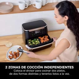 Ninja AF550EU freidora aire 6.6L negra, uso: mujer extrae cesta doble con brócoli y alitas en cocina
