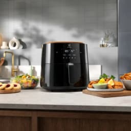 Electrolux Fritadeira de ar EAF7B 6,8L Preto, vista frontal em cozinha: painel tátil digital e alimentos ao redor
