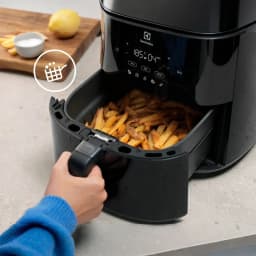 Electrolux Fritadeira ar EAF7B 6,8L preto, gaveta aberta: mão retirando cesto com batatas fritas e painel digital visível