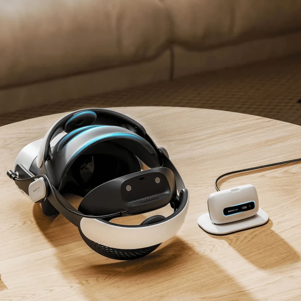 BoboVR M3 Pro+ headstrap acolchoado para VR, alça ajustável com apoio traseiro, detalhes em azul e base de carregamento compacta branca sobre mesa de madeira