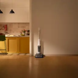 Roborock F25 RT 2,5Ah blanco, vista lateral en hogar: aspiradora apoyada en pared junto a cocina con suelo de madera