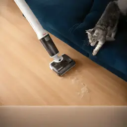 Roborock F25 RT 2,5Ah blanco, en uso: cabezal limpiando pelo de gato en suelo laminado junto a sofá azul