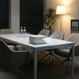 Acer Projecteur PD1810IC 4K UHD RGB-LED Blanc, vue en salle: sur table de réunion avec chaises et objectif allumé