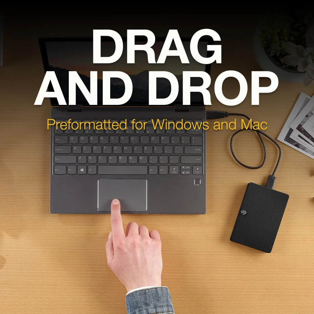 Seagate Expansion STKM1000400 1TB negro, vista lifestyle: disco conectado a portátil en escritorio, texto Drag and Drop