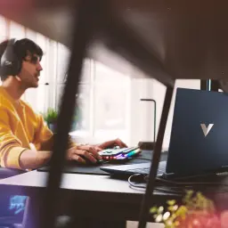 HP Victus 15 1TB Azul, vista lifestyle: gamer con auriculares usa el portátil en escritorio con teclado RGB