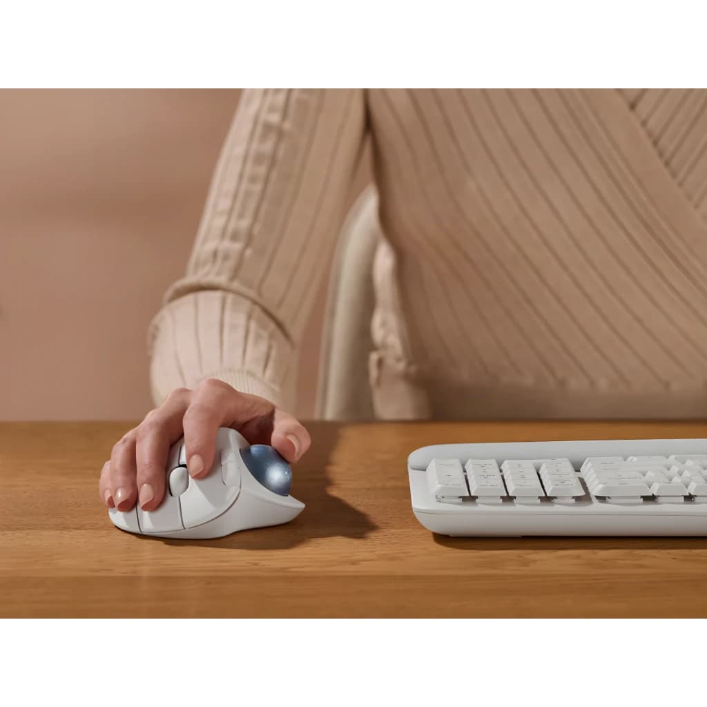 Logitech Trackball Ergo M575s blanco, uso en escritorio: mano sujetando el ratón con bola azul junto a teclado blanco