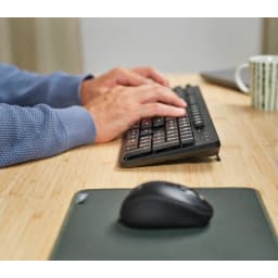 Trust TKM-360 QWERTY negro, uso en escritorio: manos escribiendo en teclado negro con ratón sobre alfombrilla en mesa