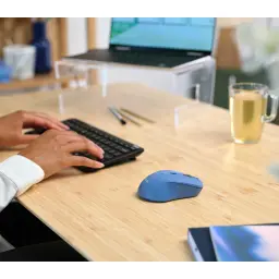 Trust Souris sans fil Mydo Silent bleue, en situation: sur bureau en bambou avec clavier et ordinateur portable