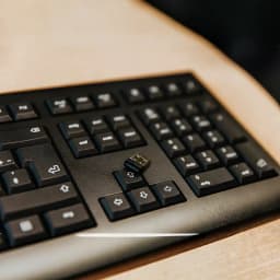 Cherry Teclado KW 3000 Inalámbrico Negro, detalle: nano receptor USB Cherry apoyado sobre las teclas en escritorio de madera