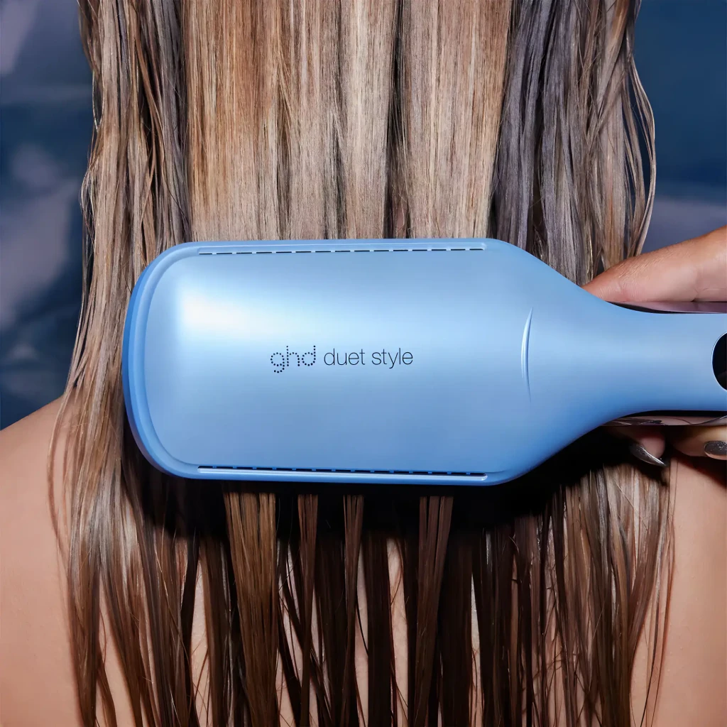 GHD Prancha Duet Style Vapor Azul, uso: vista traseira aplicada em cabelo longo loiro com mão segurando o cabo