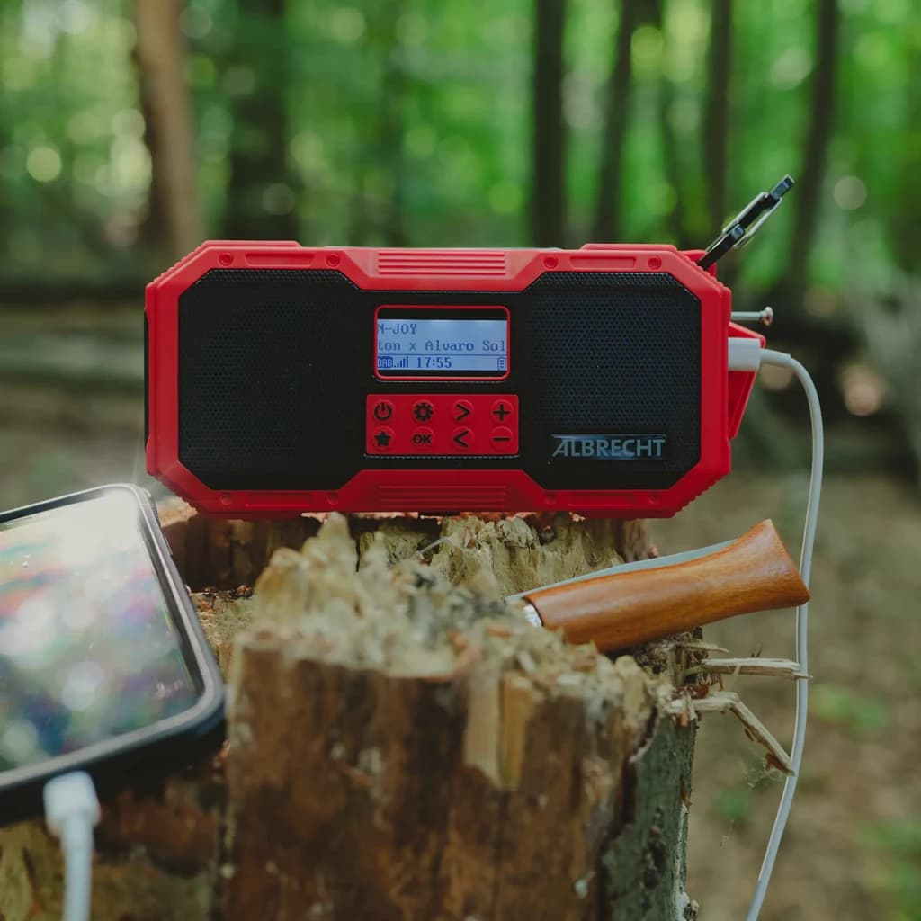 Radio Midland DR112 Outdoor Recargable DAB+, FM Batería + Solar roja sobre tronco en bosque, pantalla LCD encendida y cable