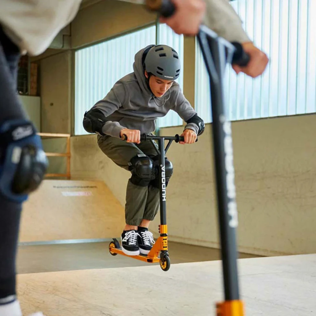 Patinete acrobático Hudora XR-25.1 Aluminio T6, ruedas PU 100mm ABEC 9 10+ Dorado/Negro, en uso: joven con casco ejecutando