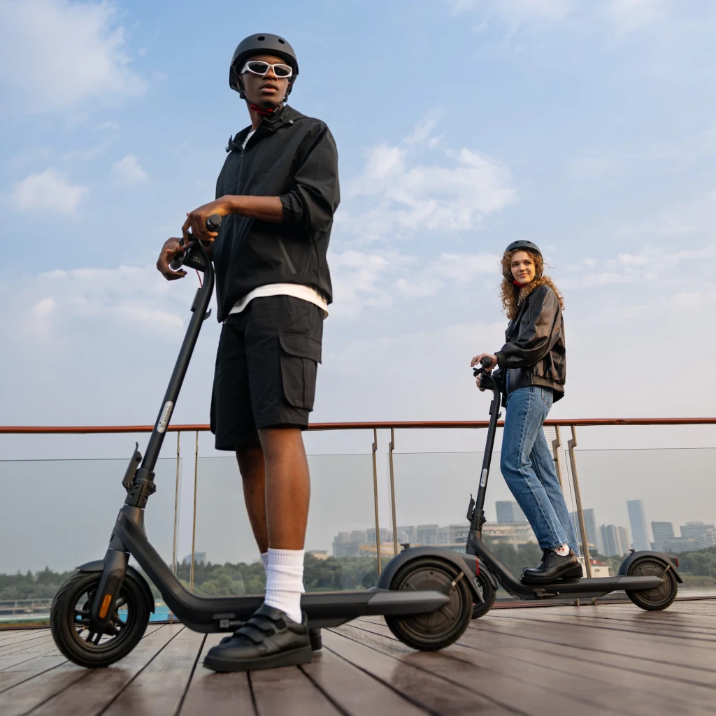 Trotinete Elétrica Ninebot by Segway KickScooter E2 Pro E Preto, em uso: duas pessoas a andar em terraço urbano com skyline
