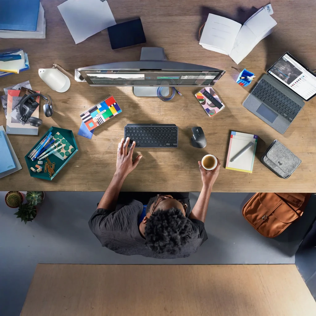 Teclado Logitech MX Keys Mini Inalámbrico Grafito, en uso: vista cenital sobre escritorio de madera con persona tecleando