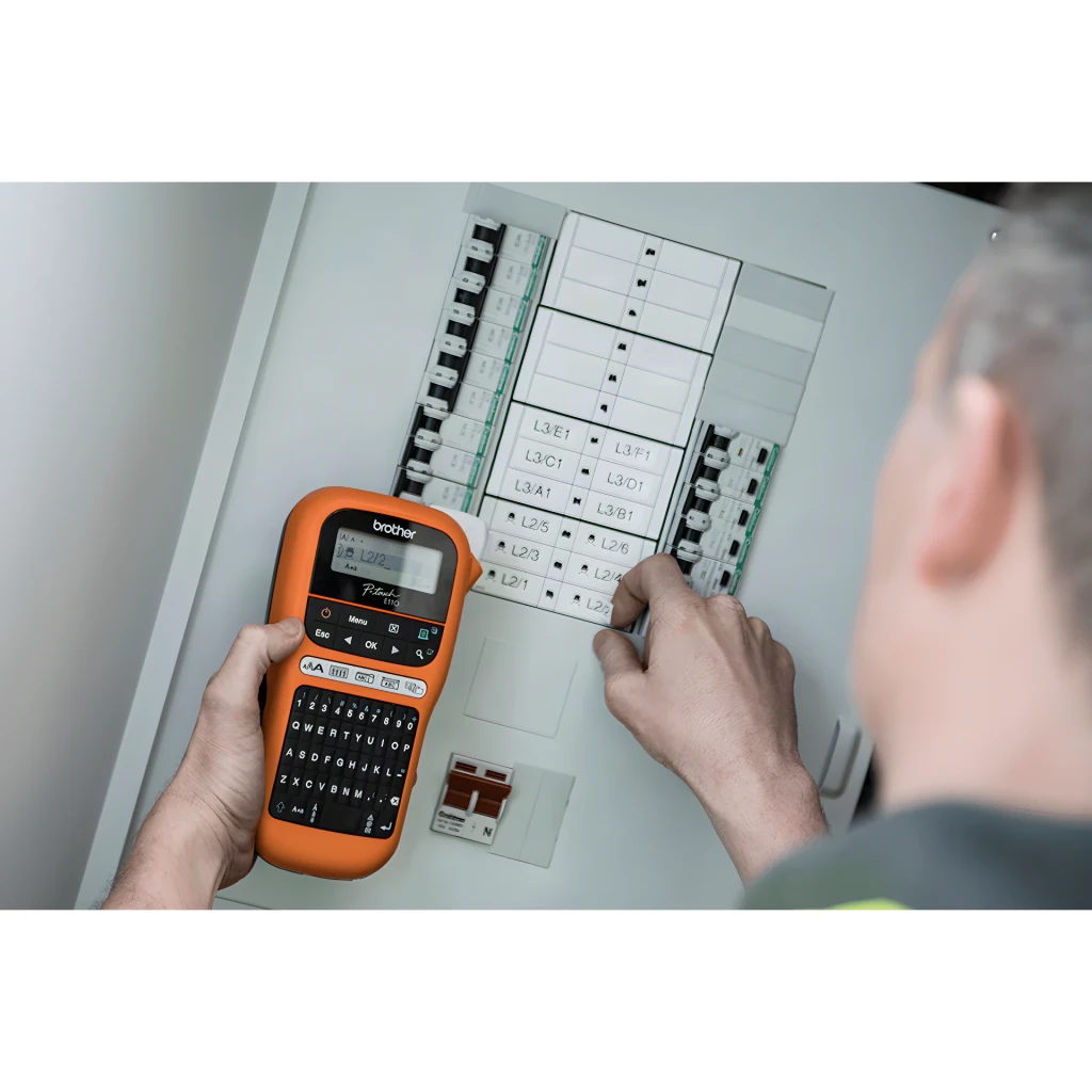 Impresora de etiquetas Brother PT-E110 Negro/Naranja, en uso: técnico etiqueta cuadro eléctrico sujetando la impresora