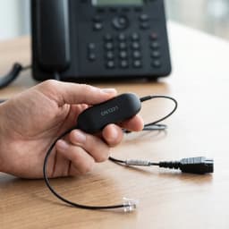 Cable auricular Jabra GN1221 Sound Limiter QD a RJ-9 0,8m Negro, en uso: mano sostiene el módulo limitador negro