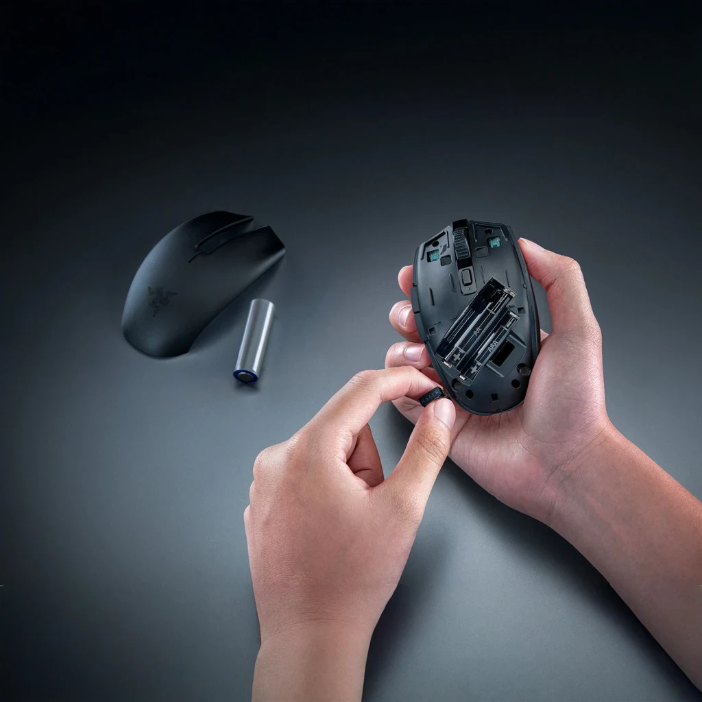 Ratón Gaming Razer Orochi V2 2026 Inalámbrico 18000 DPI Negro, en uso: manos insertando pila AA con compartimento abierto