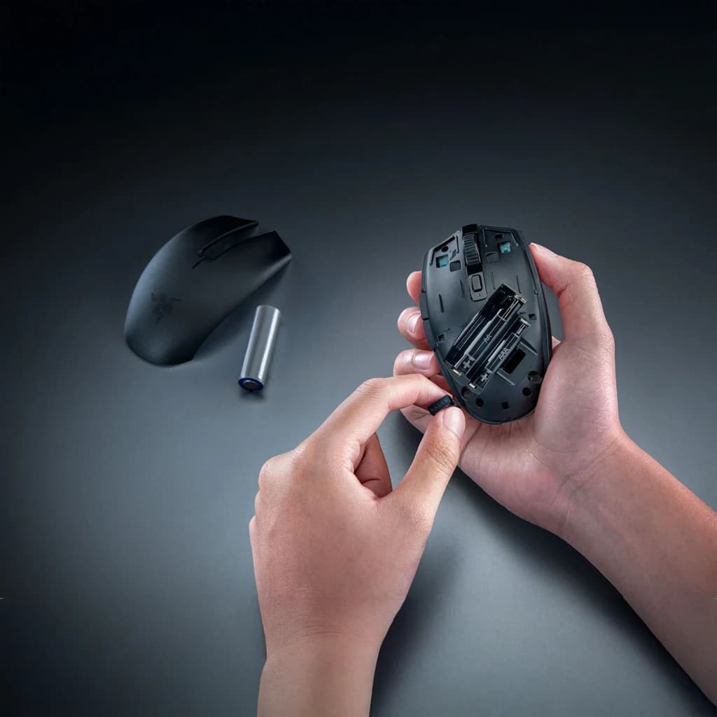 Ratón Gaming Razer Orochi V2 2026 Inalámbrico 18000 DPI Negro, en uso: manos insertando pila AA con compartimento abierto