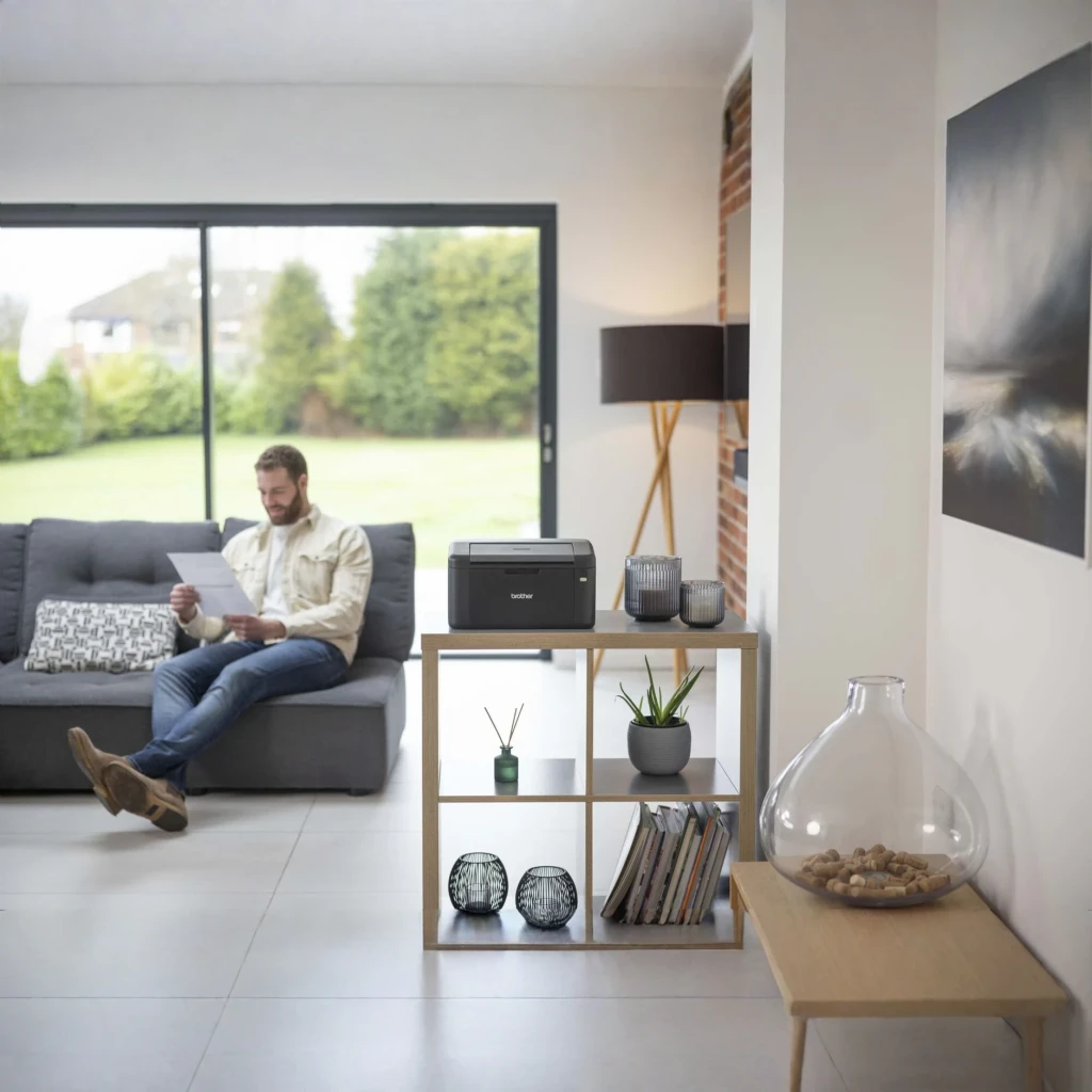 Impresora Brother HL-L1242W Láser Monocromo WiFi Dúplex Manual Negro, en uso: sobre estantería en salón, hombre al fondo