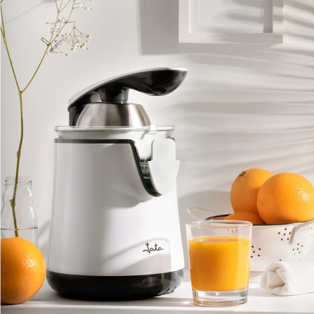 Exprimidor JATA 350W Blanco JEEX1058, en uso: sobre encimera con naranjas y vaso de zumo recién exprimido