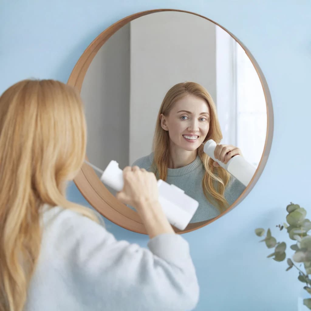 Irrigateur Oral Panasonic EW-DJ66 Sans Fil 60min Blanc, en cours d'utilisation: femme souriante devant miroir rond
