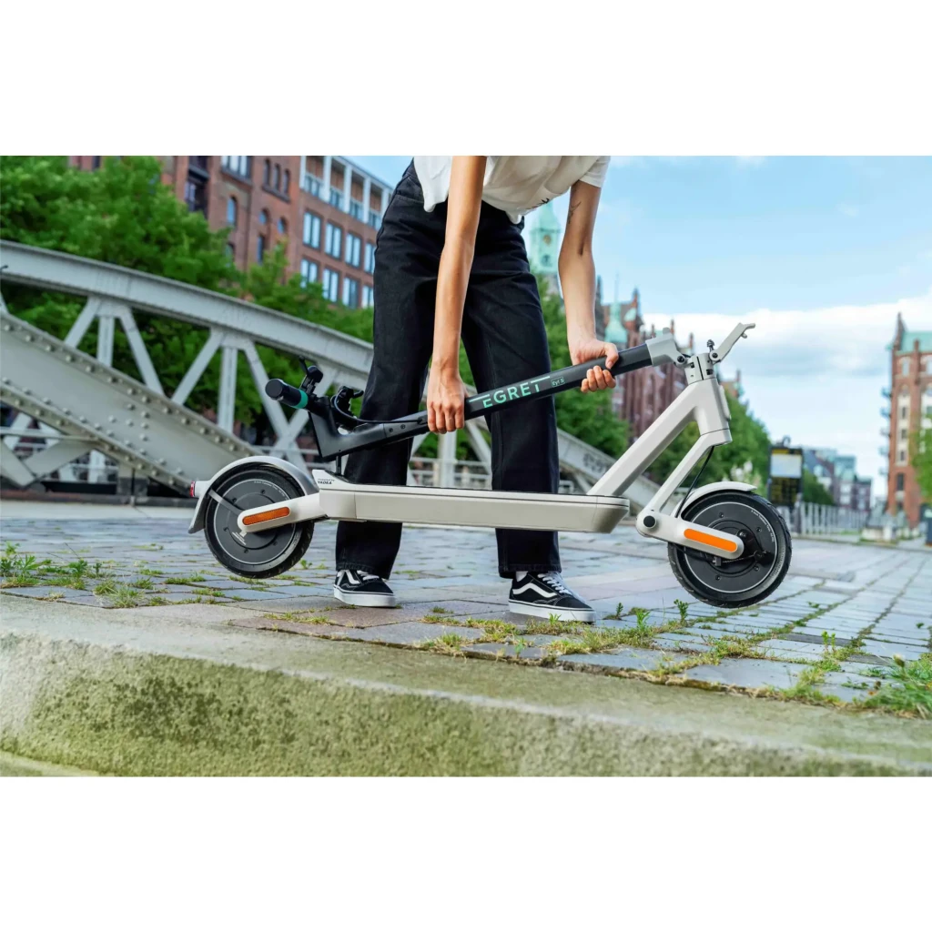Patinete eléctrico Egret Ey! 3 20km/h 9 pulgadas Gris, en uso: persona transportándolo plegado por adoquines urbanos