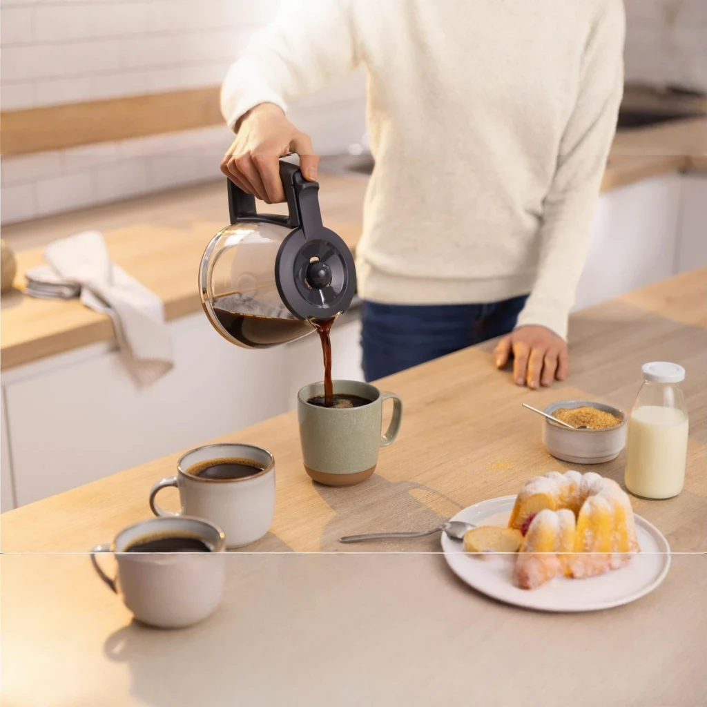 Cafeteira de filtro Bosch MyMoment 1,25L 1200W Branco TKA3M131, em uso: jarra de vidro a servir café em caneca sobre bancada