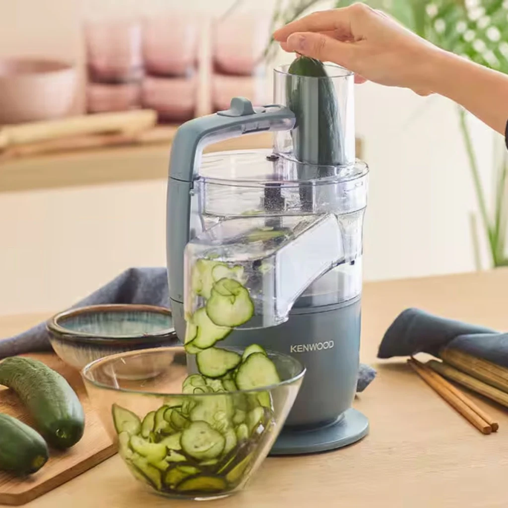 Robot de cozinha Kenwood MultiPro Go 1,3L 650W Azul FDP22.130GY, em uso: mão a introduzir pepino pelo tubo, rodelas a cair
